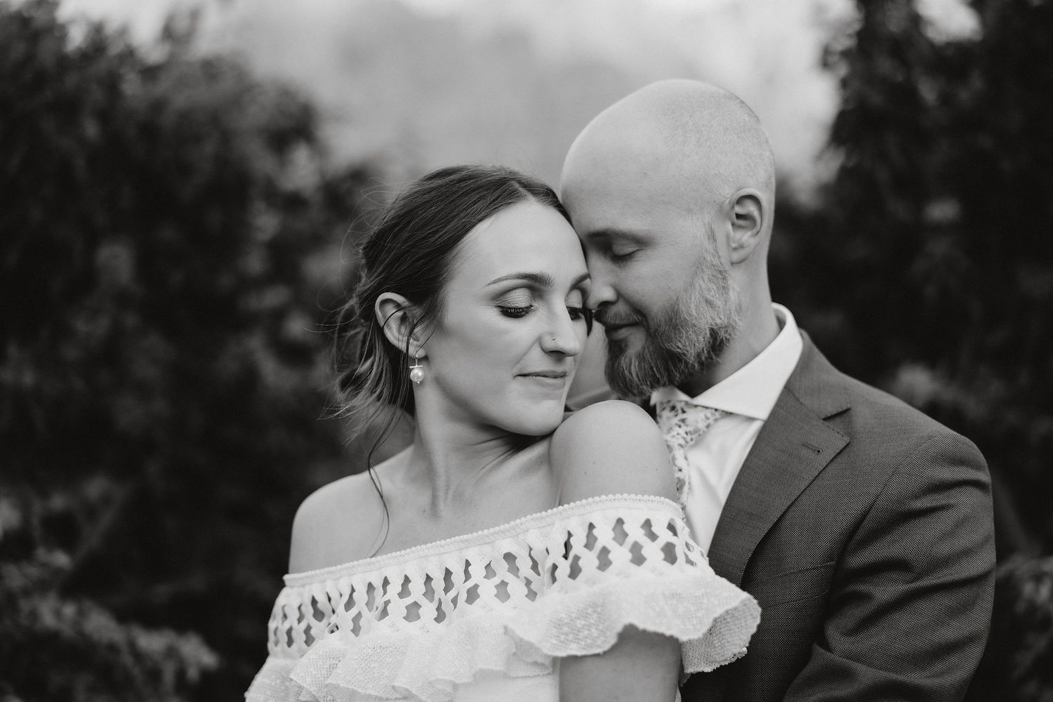 A romantic black and white portrait of a couple in an intimate embrace outdoors, with soft lighting and natural scenery.