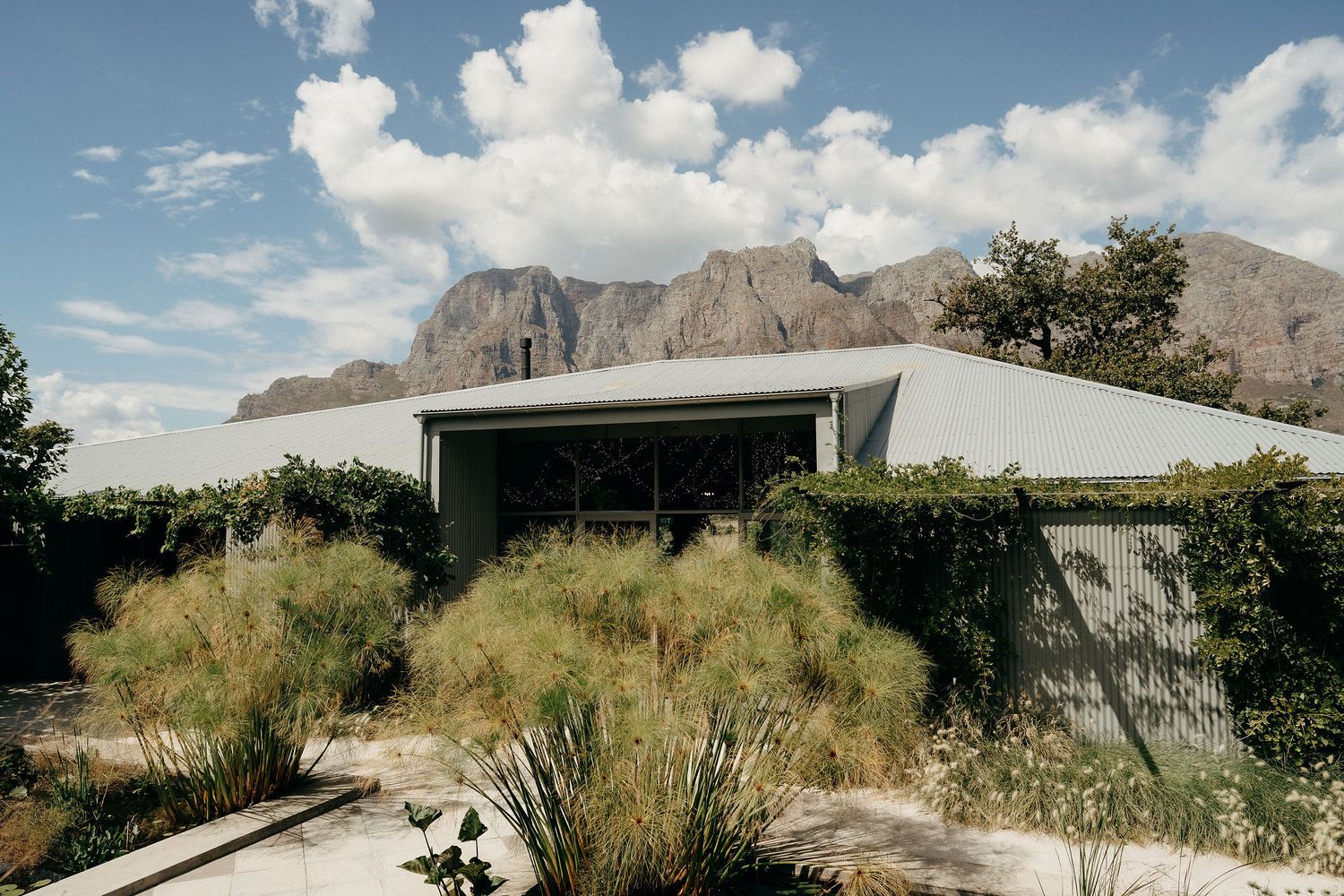 Modern minimalist house with desert landscaping and mountain backdrop under blue skies in arid environment.