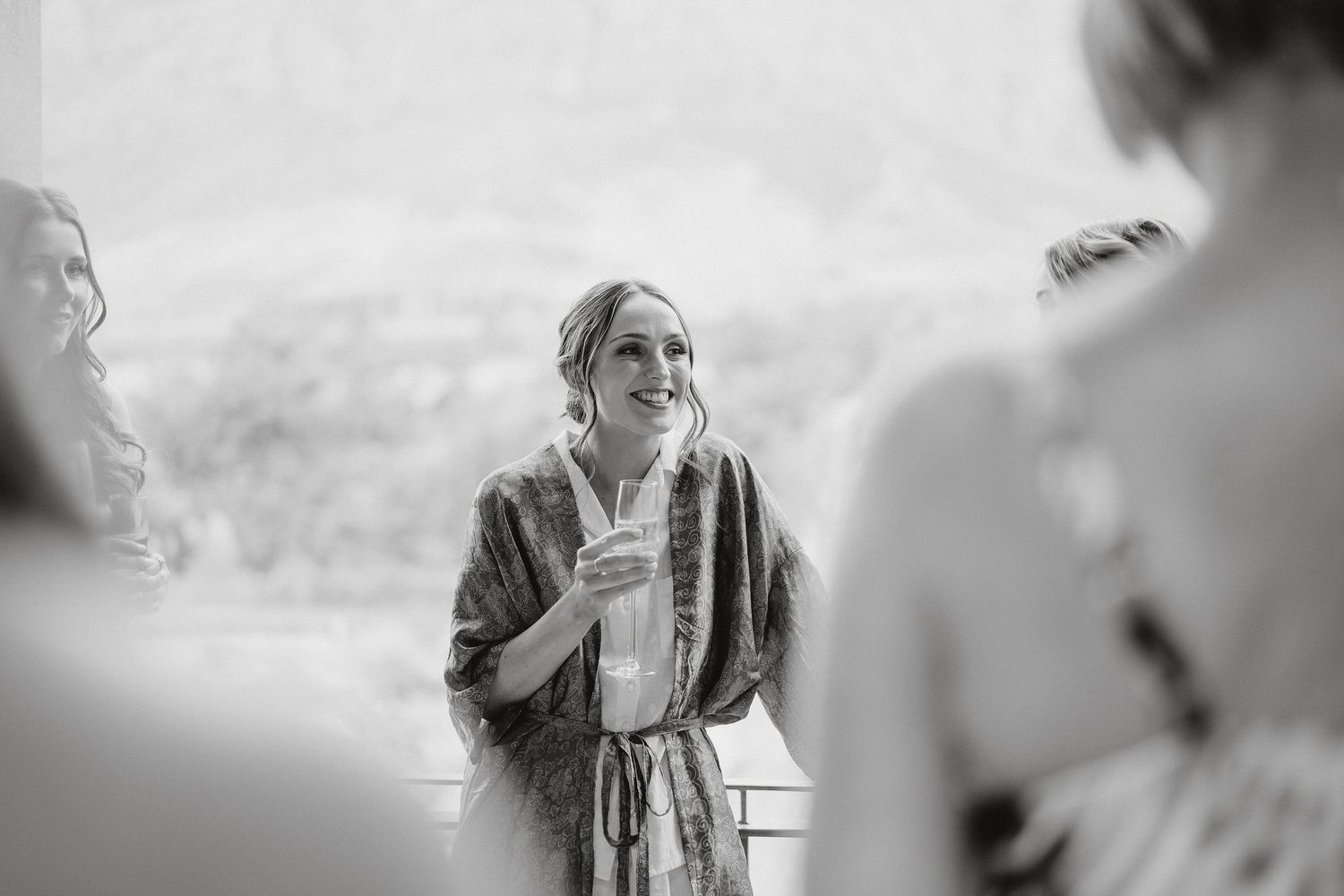 Black and white candid photo of someone in a robe holding a glass while engaged in conversation.