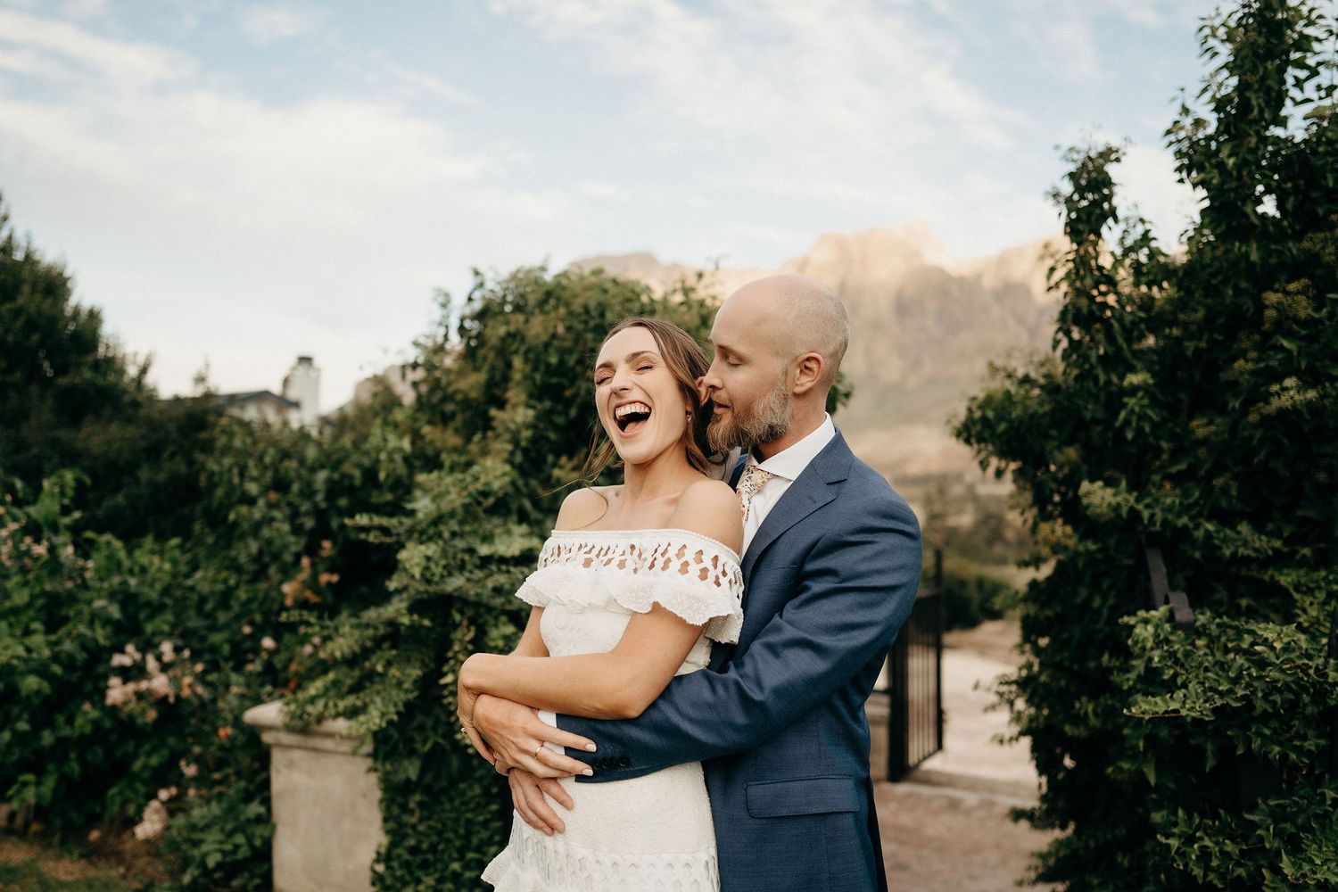 Happy couple sharing a joyful moment in a lush garden setting with mountains in the background.