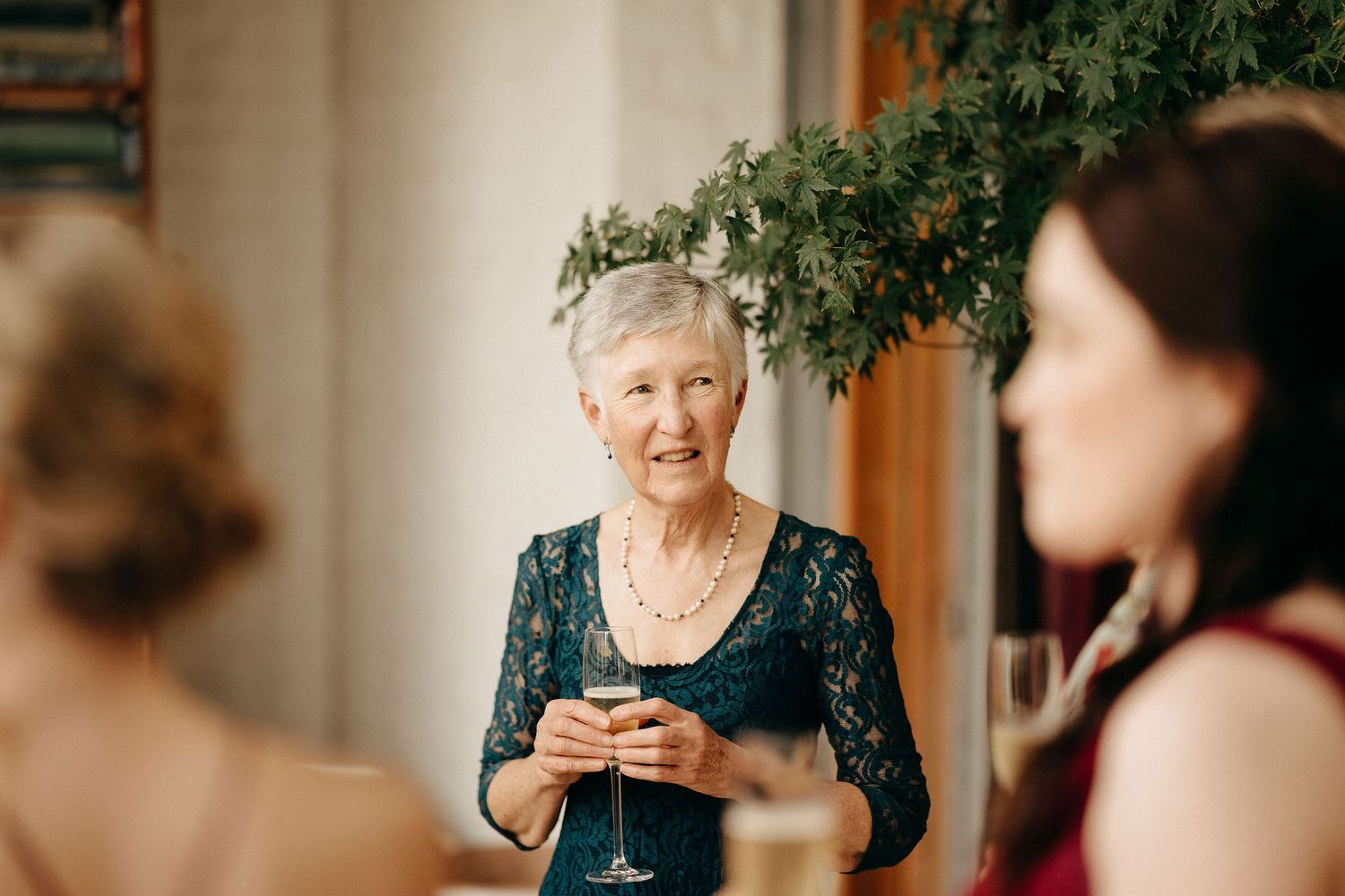 A person in a navy blue lace dress holds a drink while engaged in conversation at a social gathering.