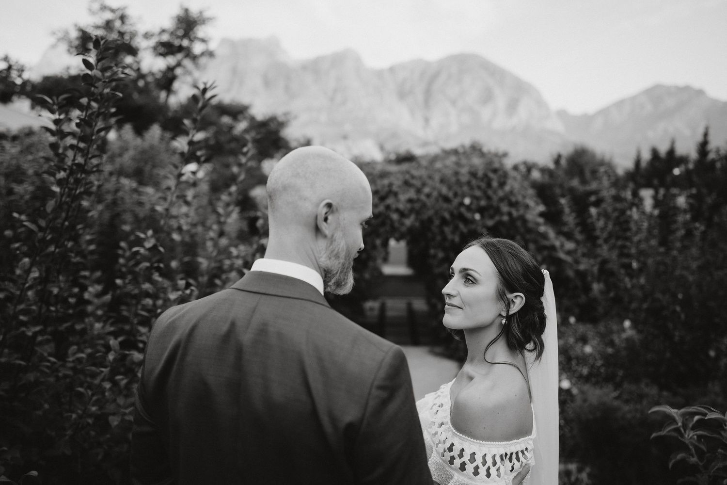 Black and white romantic moment captured between couple outdoors with majestic mountains in background.