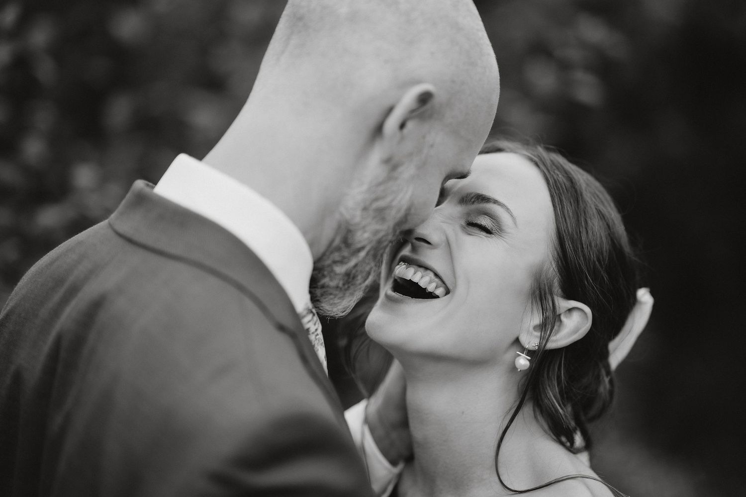 Black and white candid photo showing joyful wedding moment with bride laughing during intimate moment with groom.