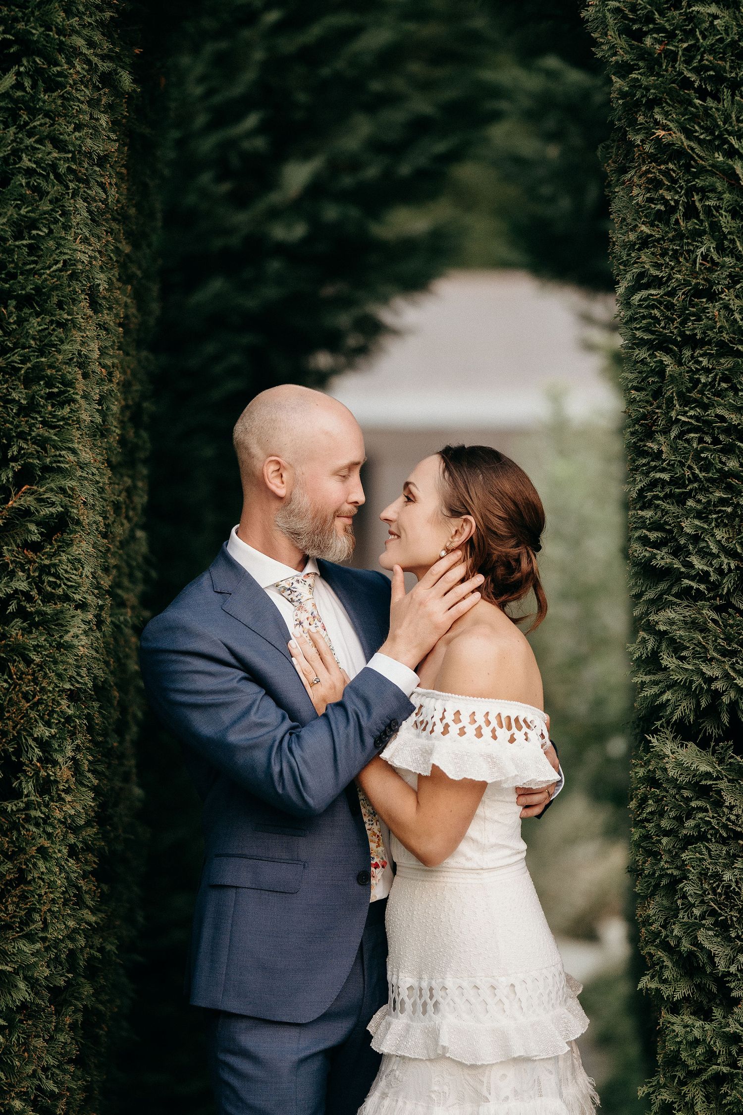 Romantic wedding couple embraces in a garden archway surrounded by lush green hedges.