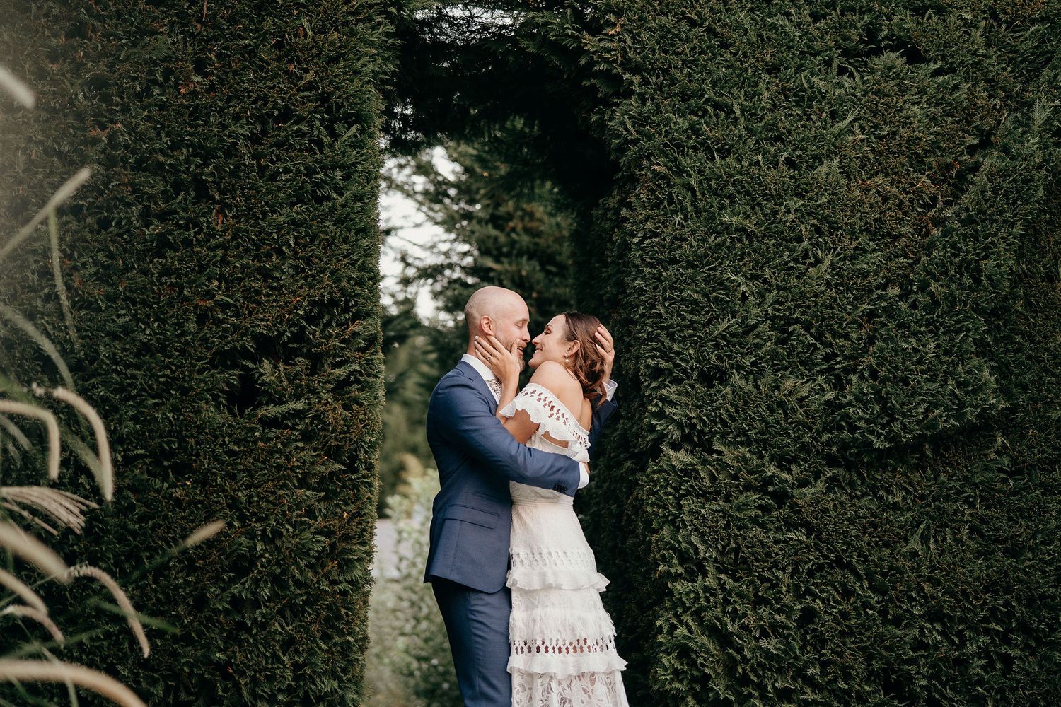 A romantic wedding couple embraces in a lush garden archway with ivy-covered walls.