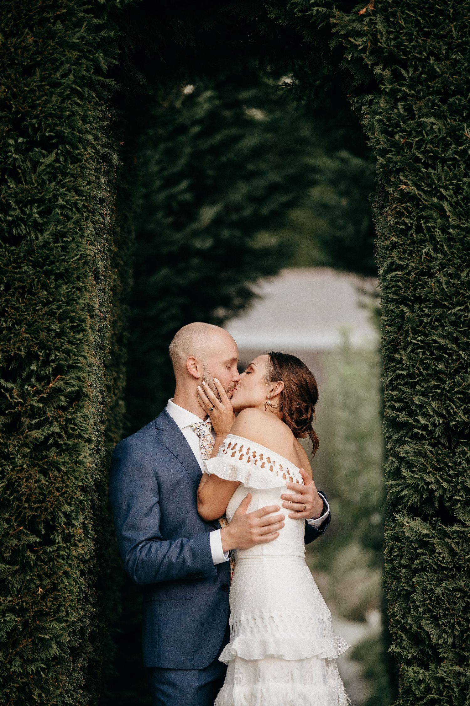 Romantic couple sharing a kiss in a garden archway framed by lush green hedges.