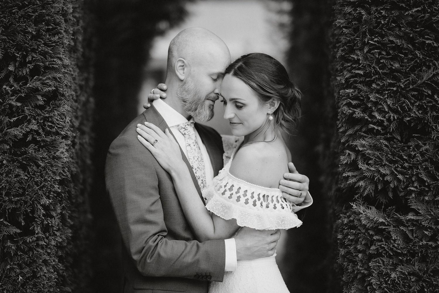 A bride and groom share an intimate black and white moment while embracing in a garden setting.