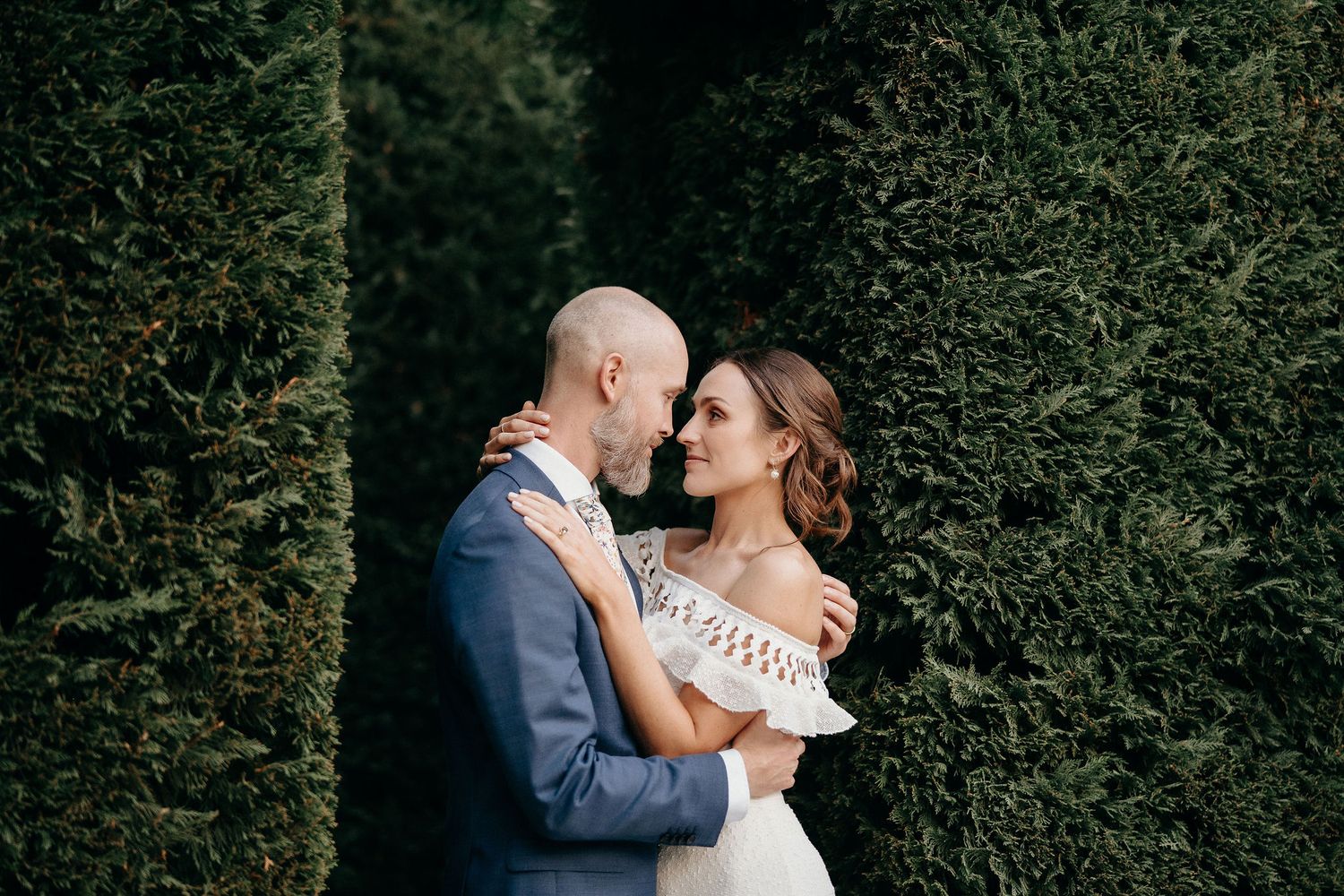 Wedding couple shares a romantic embrace among manicured garden hedges.