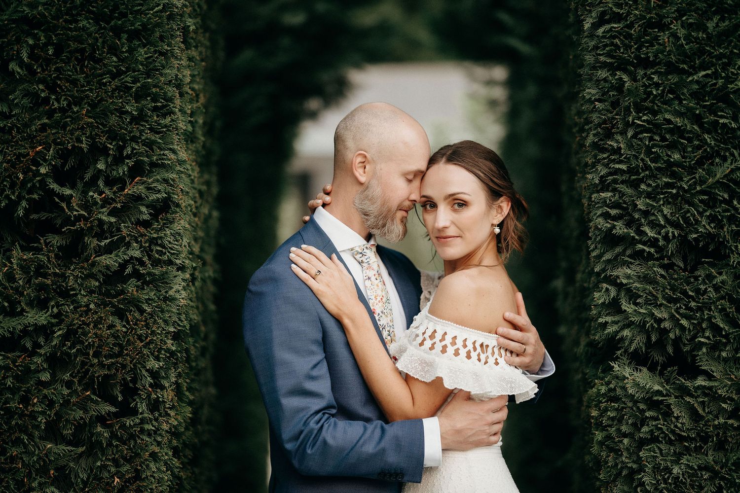 Intimate portrait of newlyweds in a formal garden with towering green hedges.