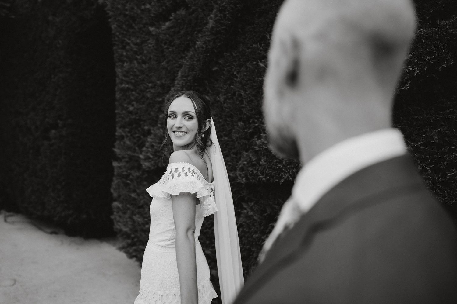 Black and white wedding photo showing candid moment with bride looking back over shoulder while wearing elegant veil.