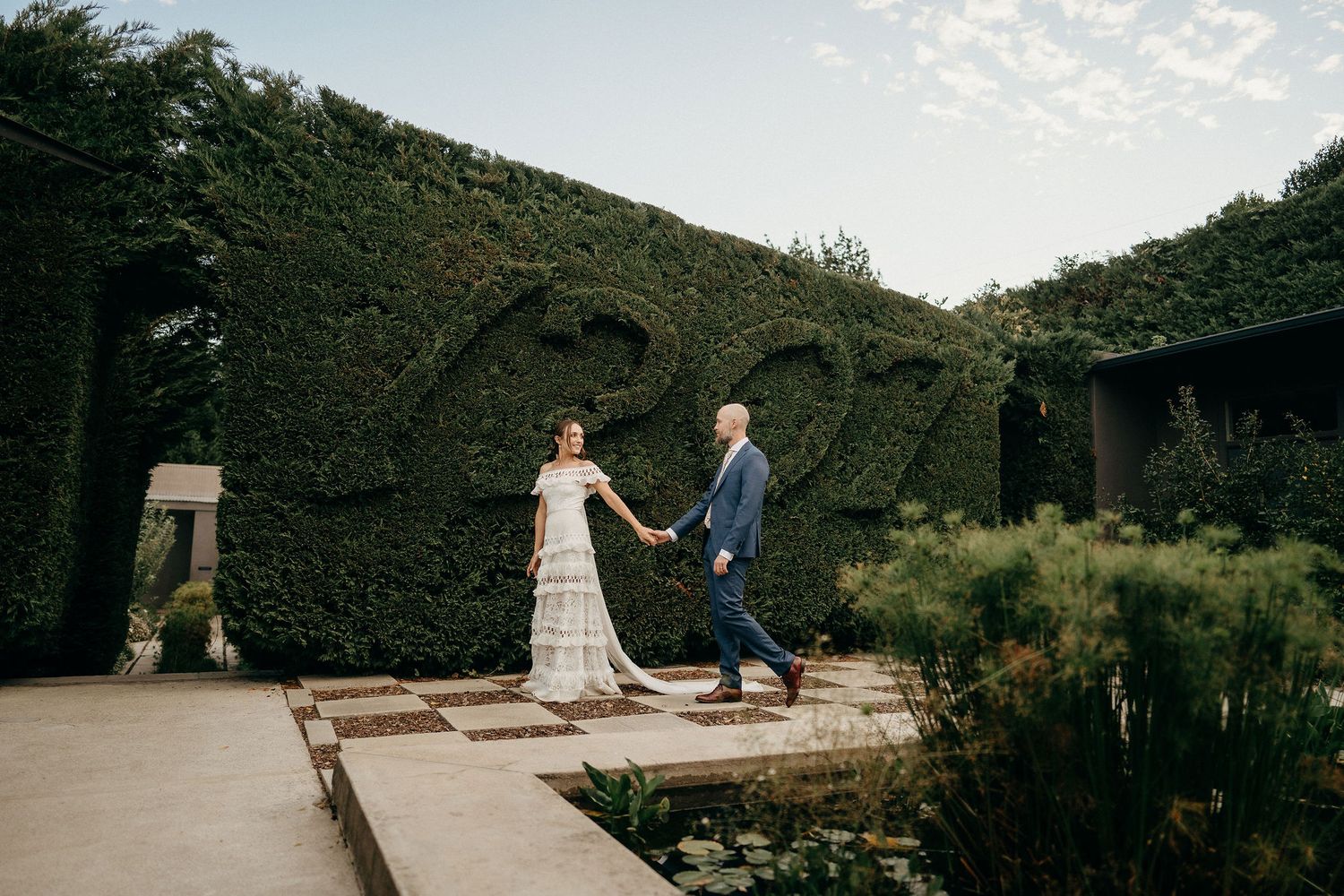 A romantic garden ceremony unfolds on a stone patio surrounded by lush ivy-covered walls under a cloudy sky.