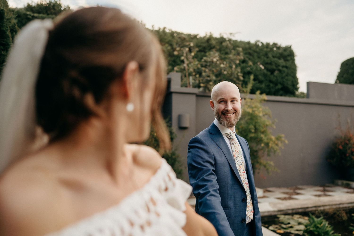A couple shares a romantic moment in front of a modern wall with greenery.