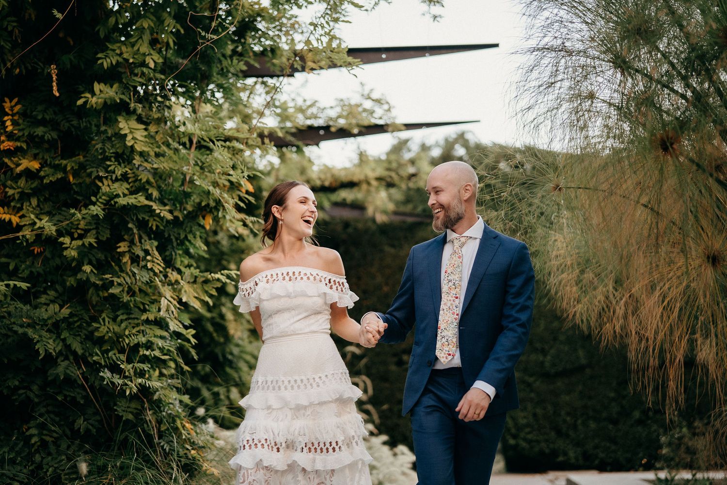 A couple shares a joyful moment in a lush garden setting during their wedding celebration.