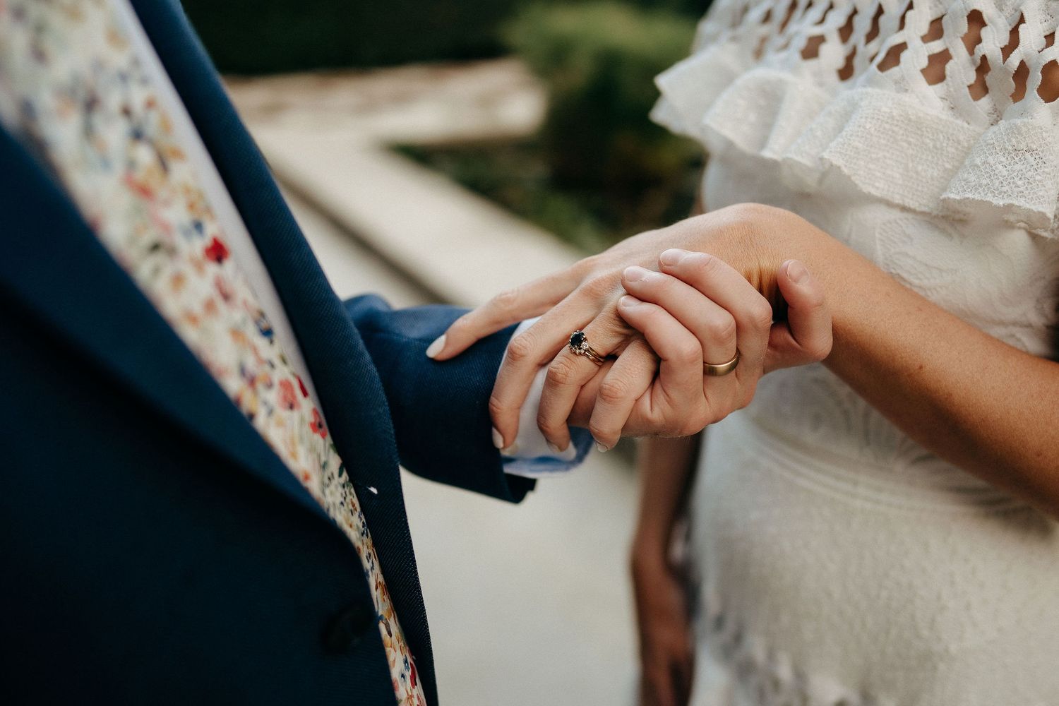 Close up of bride and groom holding hands, showing delicate lace dress details and navy suit sleeve.