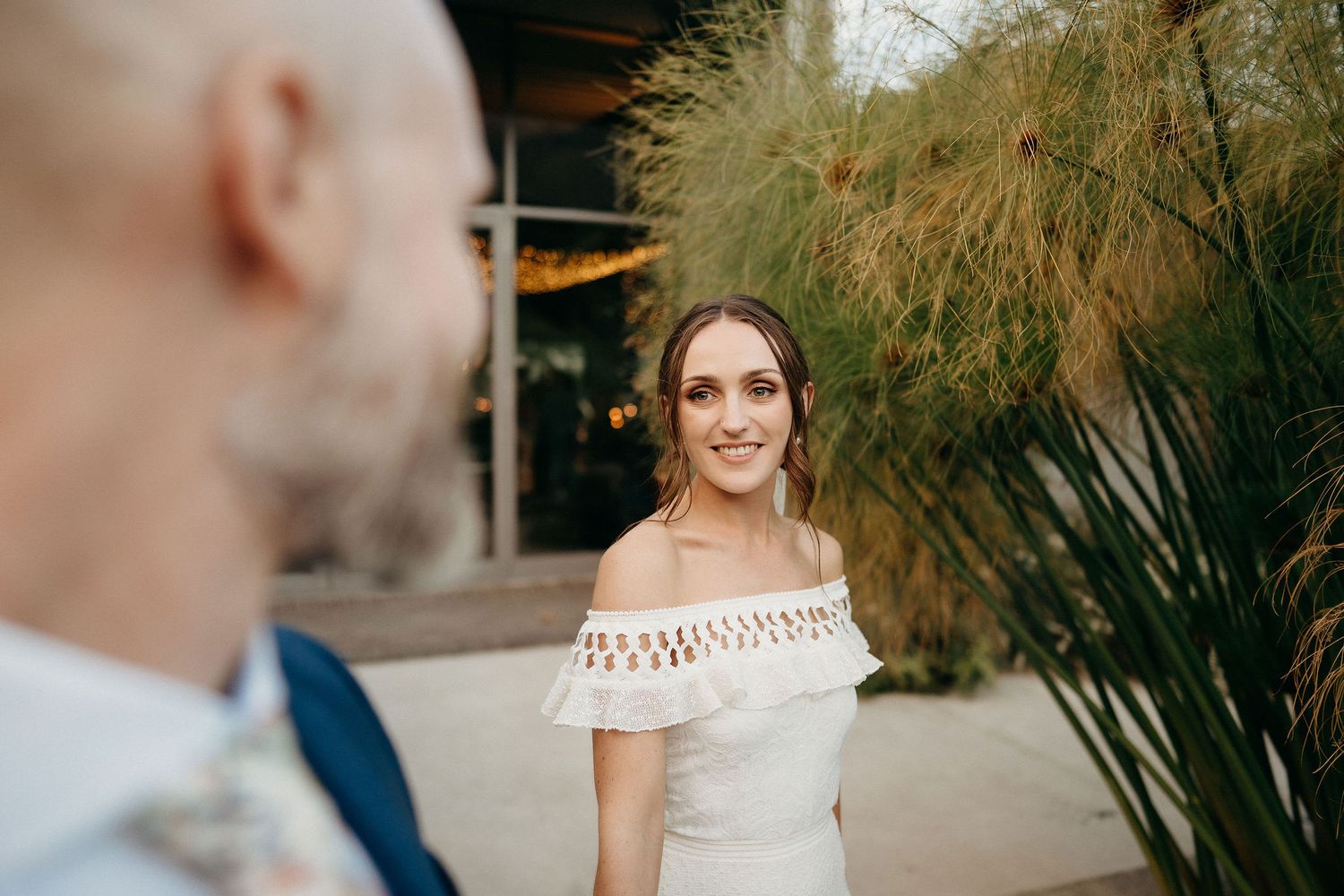 A couple shares a loving moment amongst decorative pampas grass at an elegant outdoor venue.