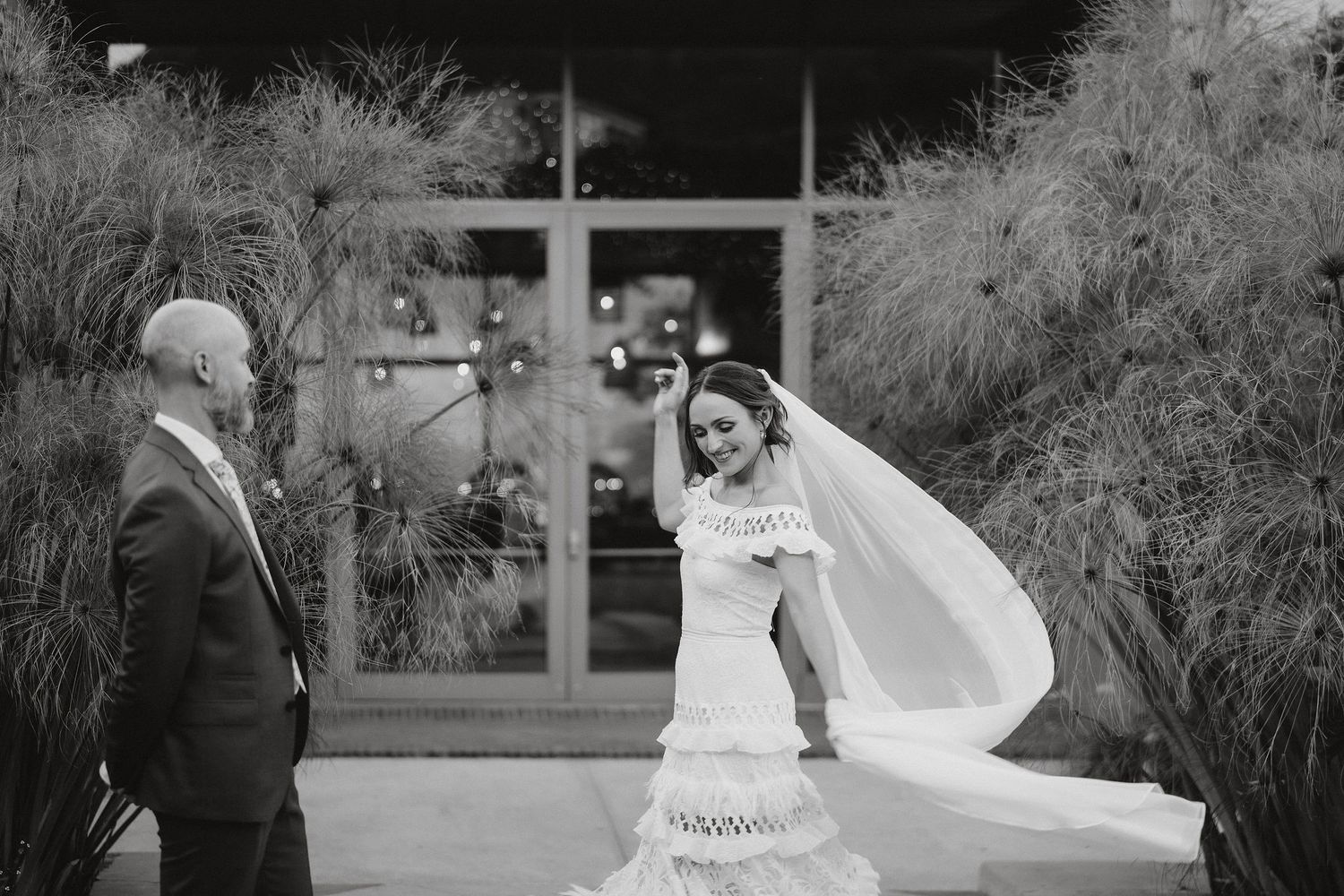 A joyful moment is captured in black and white as a flowing veil catches the breeze during an outdoor wedding celebration.