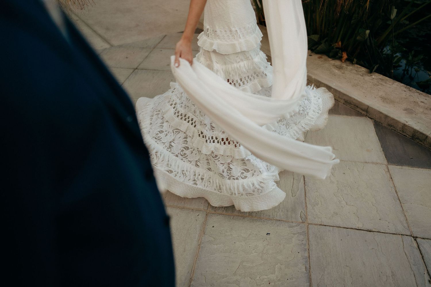 Close-up of an ornate white lace wedding dress with delicate details as it flows onto stone pavement.