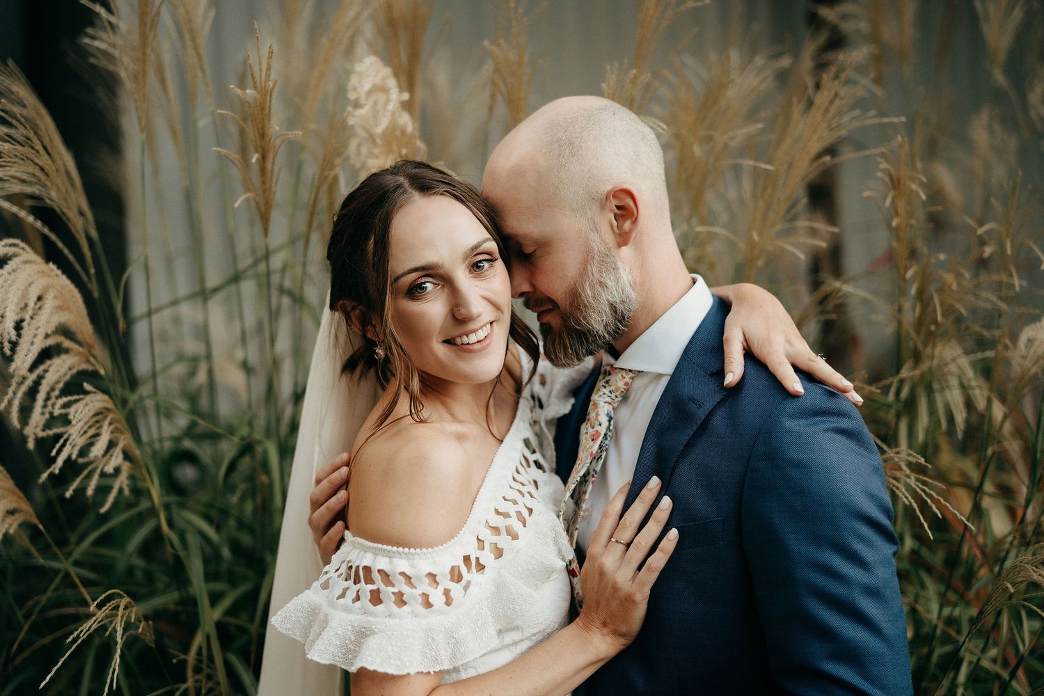 Intimate outdoor wedding portrait with couple embracing and smiling among tall pampas grass.