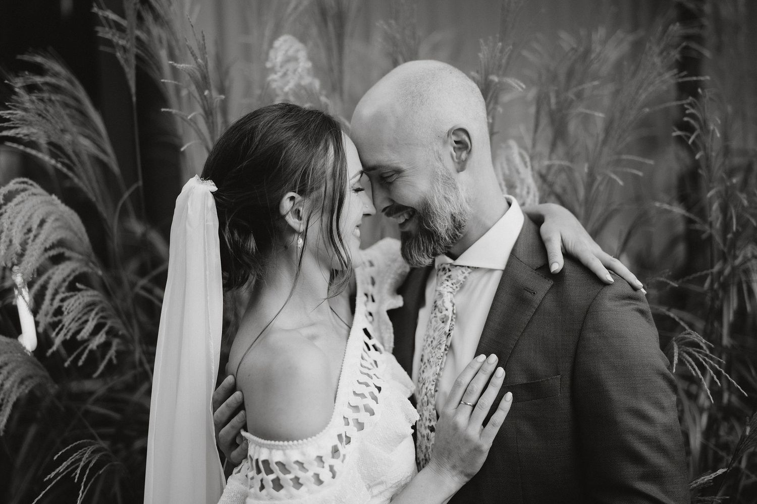 A tender black and white wedding moment captured in front of lush palm fronds.