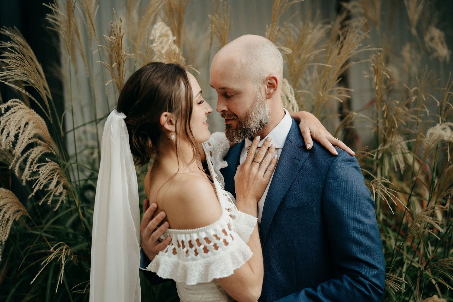 A romantic wedding moment captured between newlyweds against a backdrop of tall pampas grass.