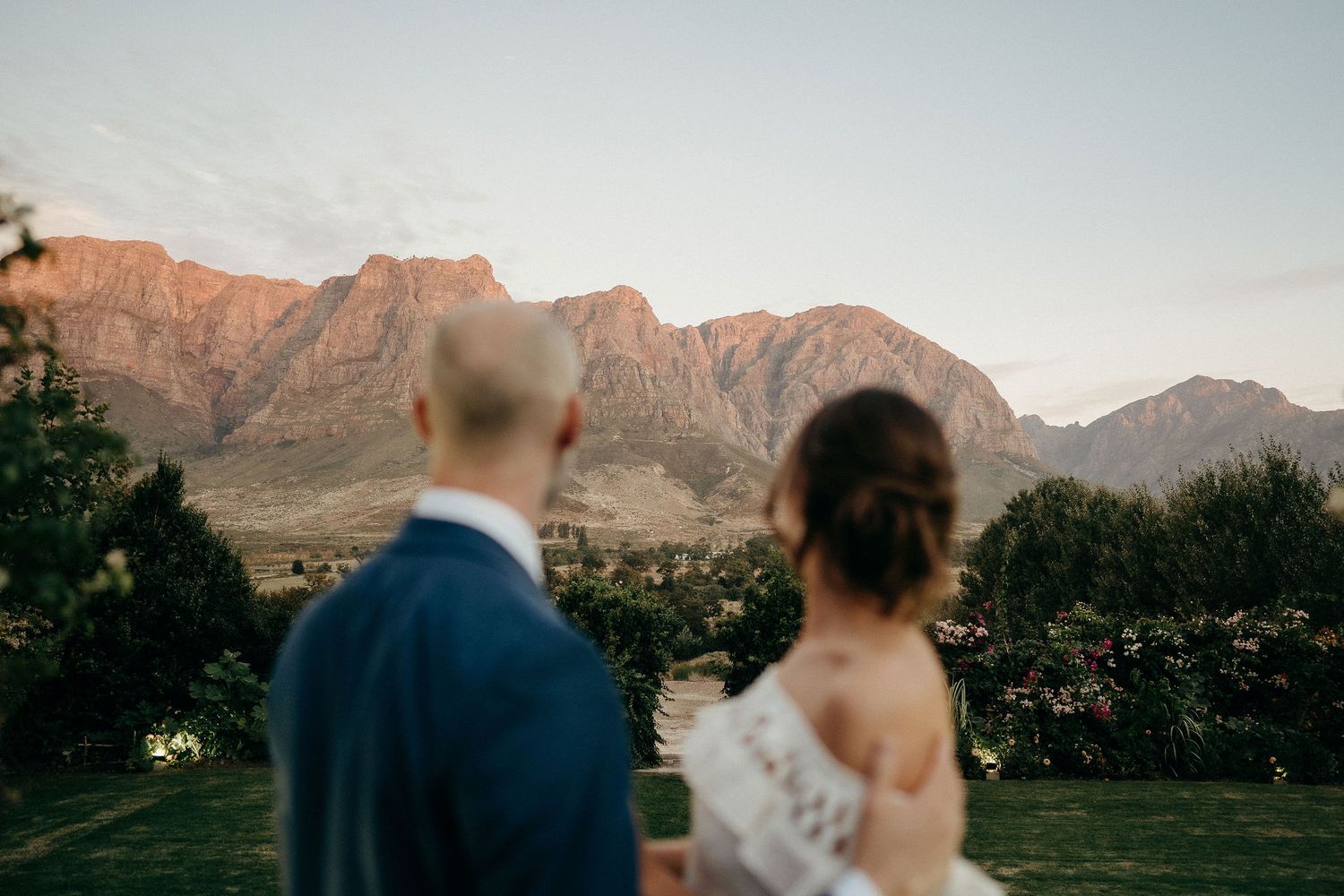 A couple looks out at majestic mountain peaks during a sunset wedding ceremony in a picturesque outdoor setting.