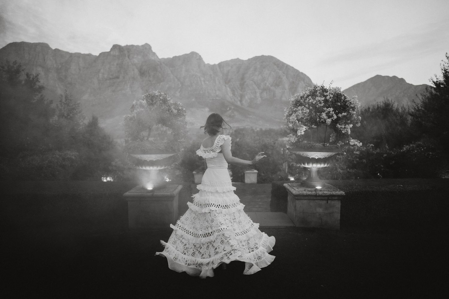 A person in an elegant white wedding dress spins in front of misty mountains during an outdoor ceremony.