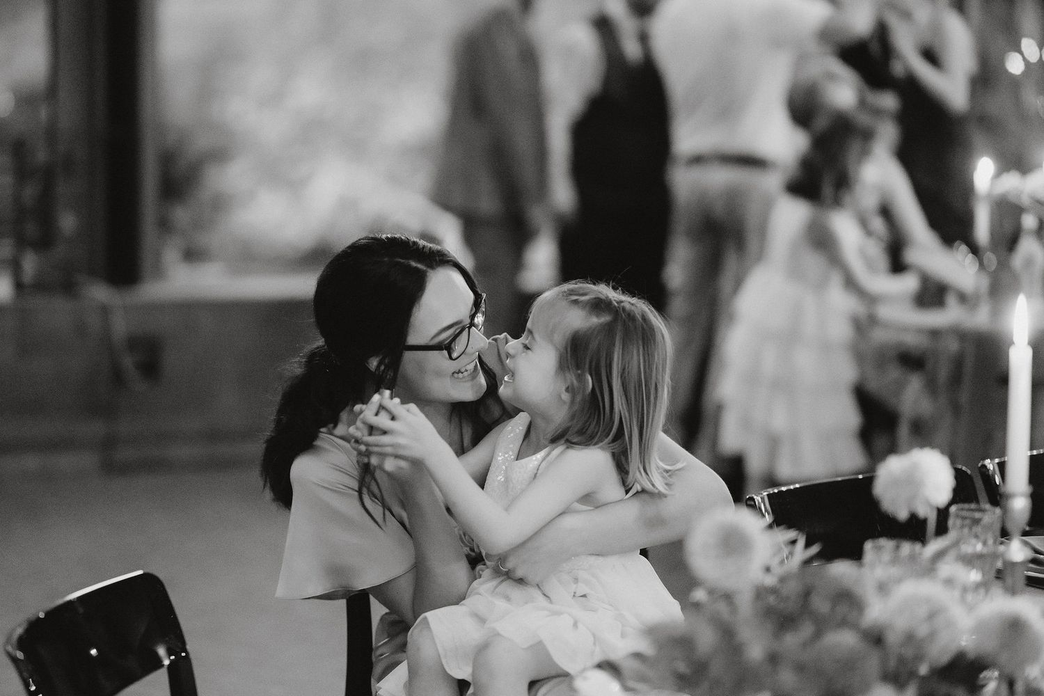 Two people share an intimate candid black and white moment at an elegant dinner table setting.