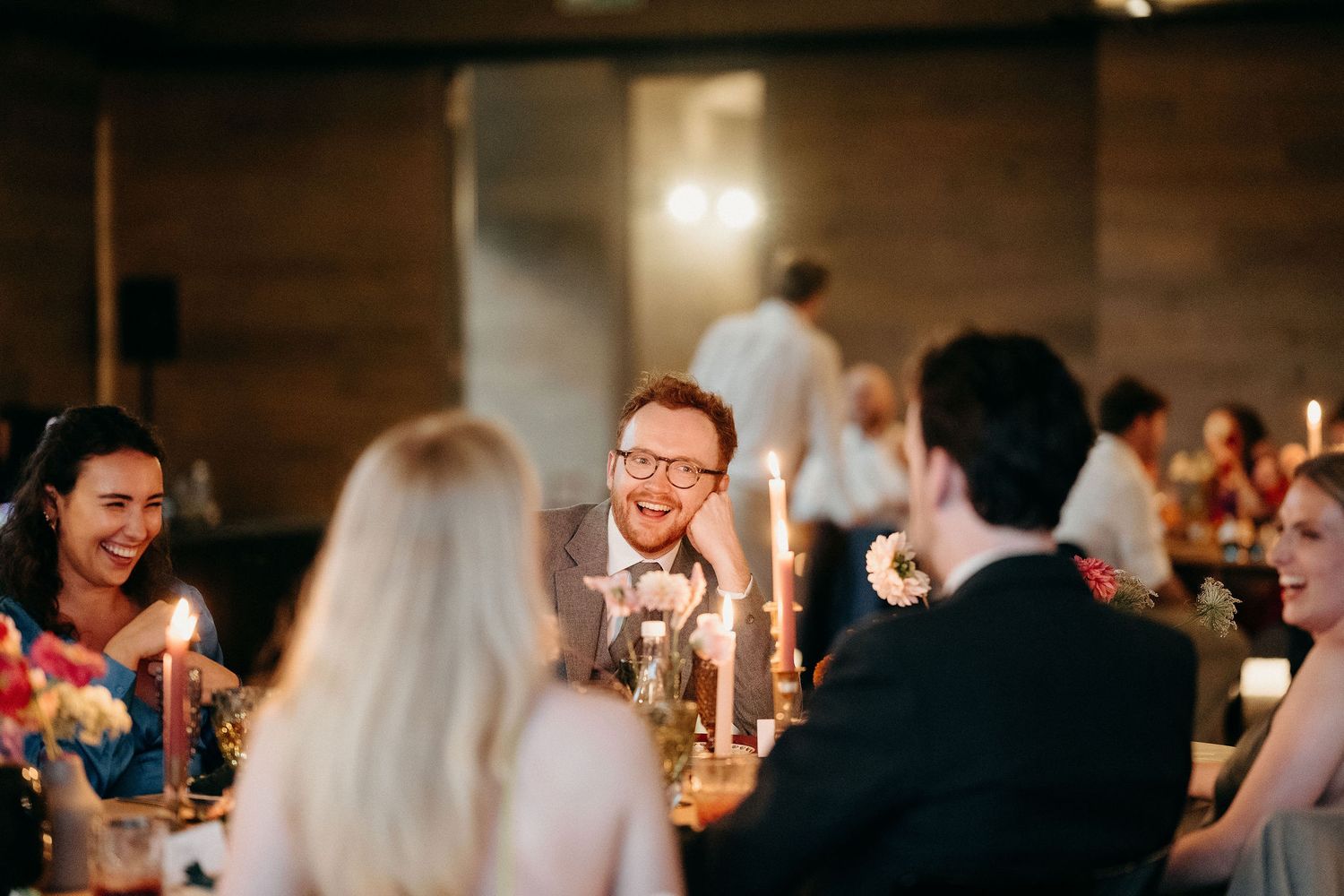 Guests sharing laughter and conversation around a candlelit dinner table at an evening reception.