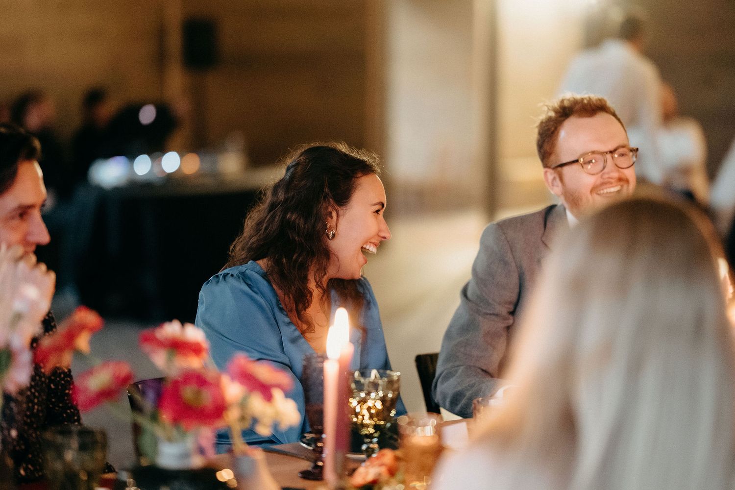 People enjoying an intimate dinner party with candlelight and flowers on the table at night.