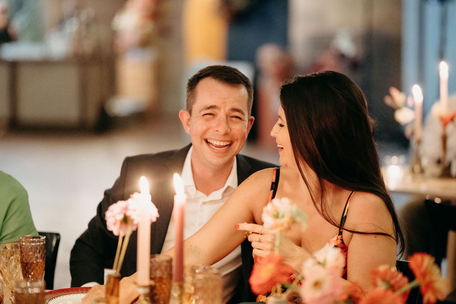 A couple shares an intimate moment while dining at a candlelit table with festive drinks and decorations.