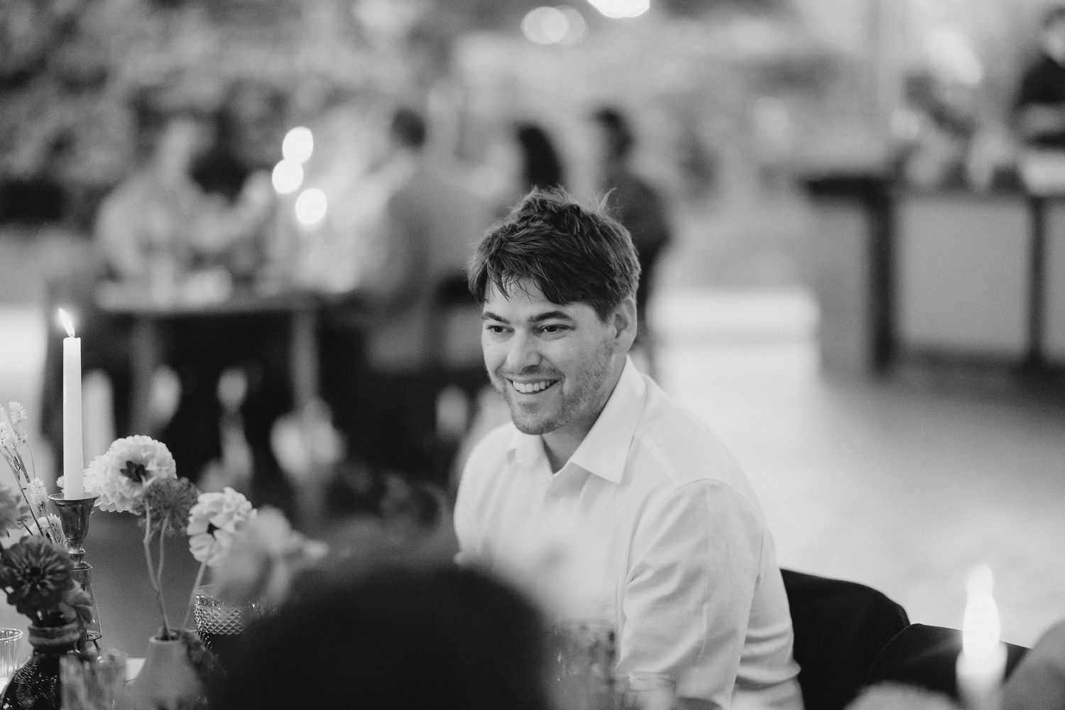 A person enjoying conversation at an elegant candlelit dinner gathering with a warm expression.