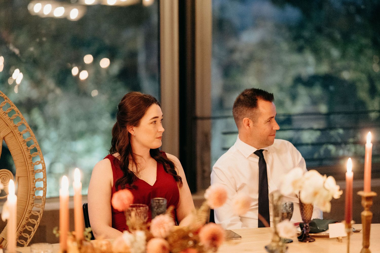 Elegant couple seated at candlelit dinner table with ornate decorations and soft lighting through window.