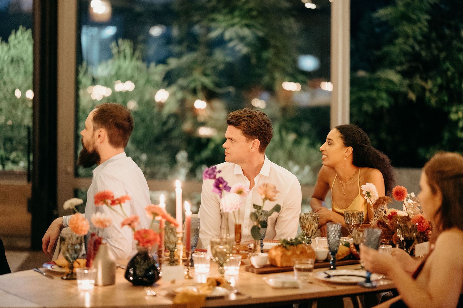 Wedding guests enjoying an intimate candlelit dinner reception with floral centerpieces and candles at a cozy indoor venue.