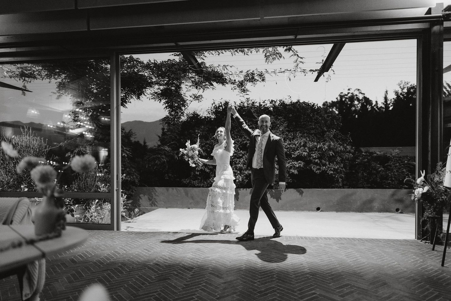 A black and white photo captures a couple joyfully dancing together on an outdoor patio during a wedding reception.