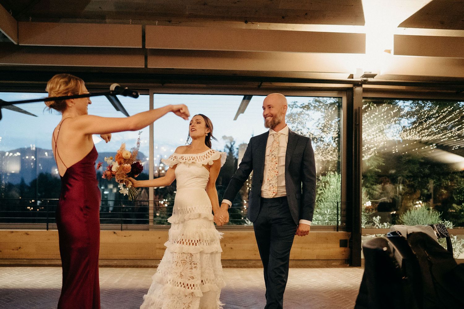 Three people dance together during a wedding celebration in a warmly lit covered outdoor venue.