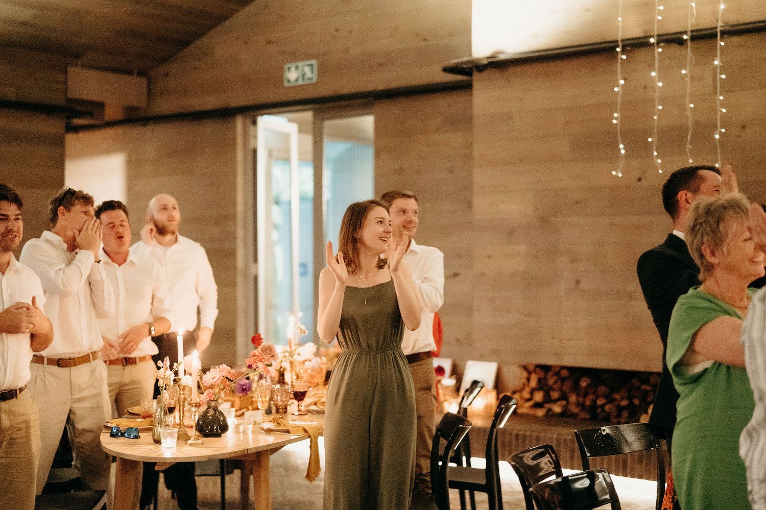 People enjoying a festive celebration in a rustic venue with candlelit tables and hanging string lights.