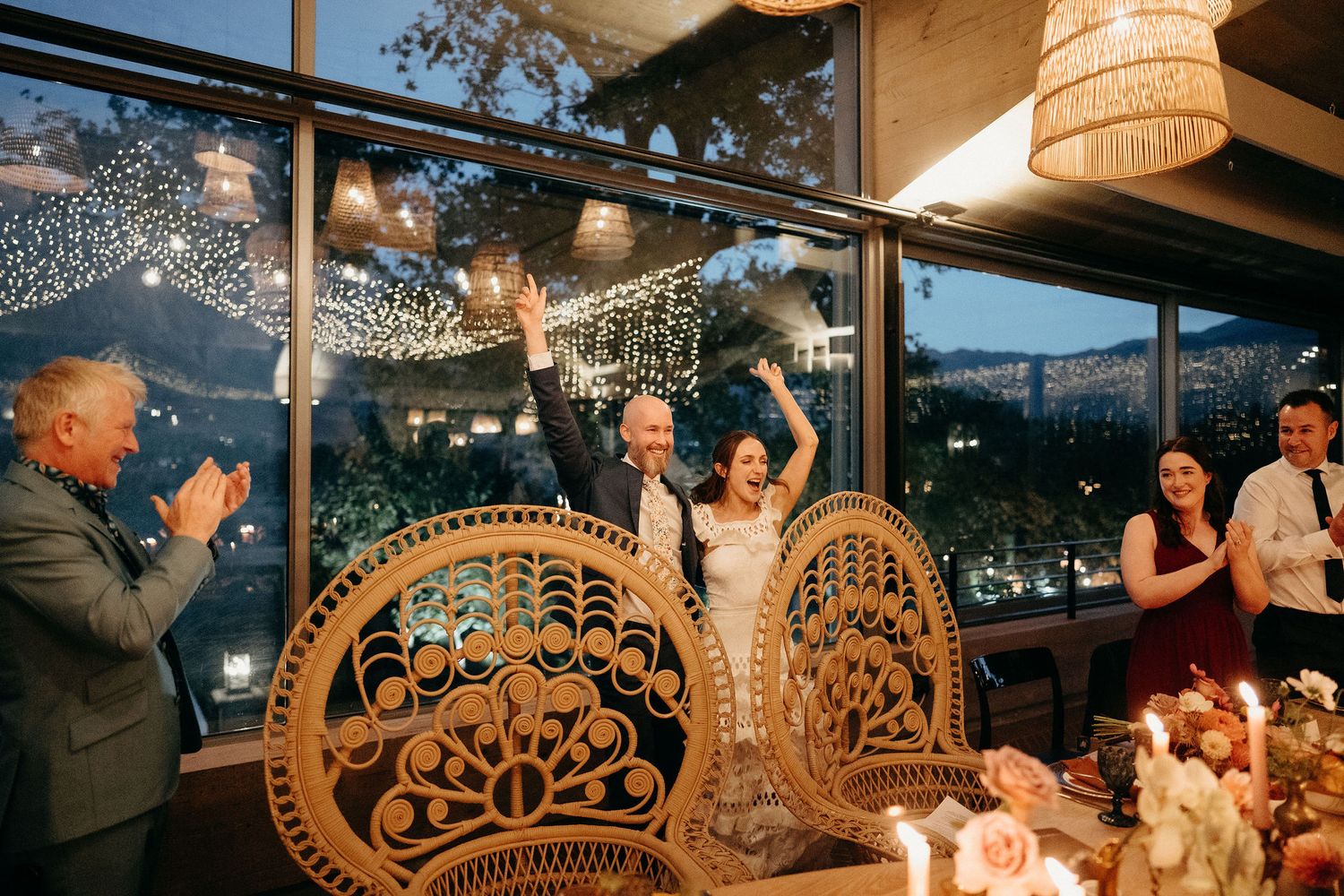Celebratory moment at wedding reception with decorative peacock chairs and string lights creating magical atmosphere.