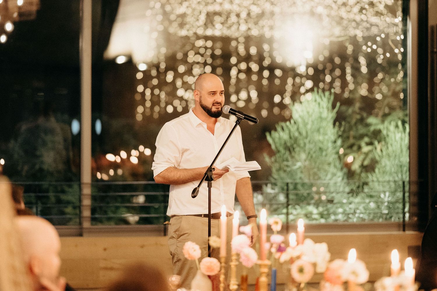 A speaker delivers remarks at an intimate candlelit reception with twinkling lights in the background.