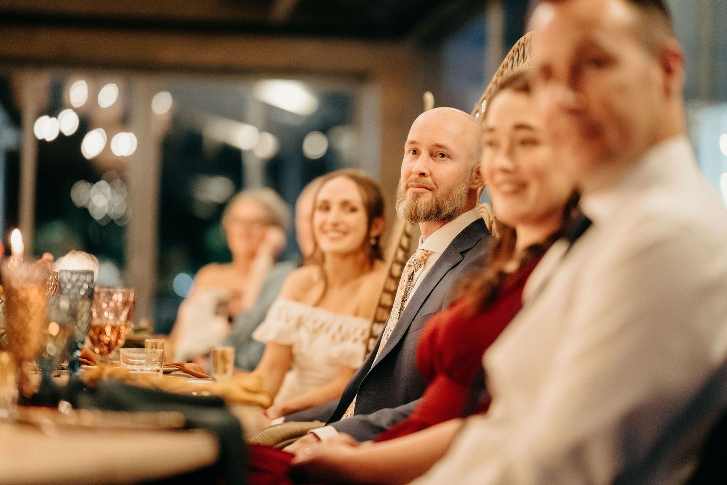 A group of people at a dinner party sitting together and enjoying conversation in warm lighting.