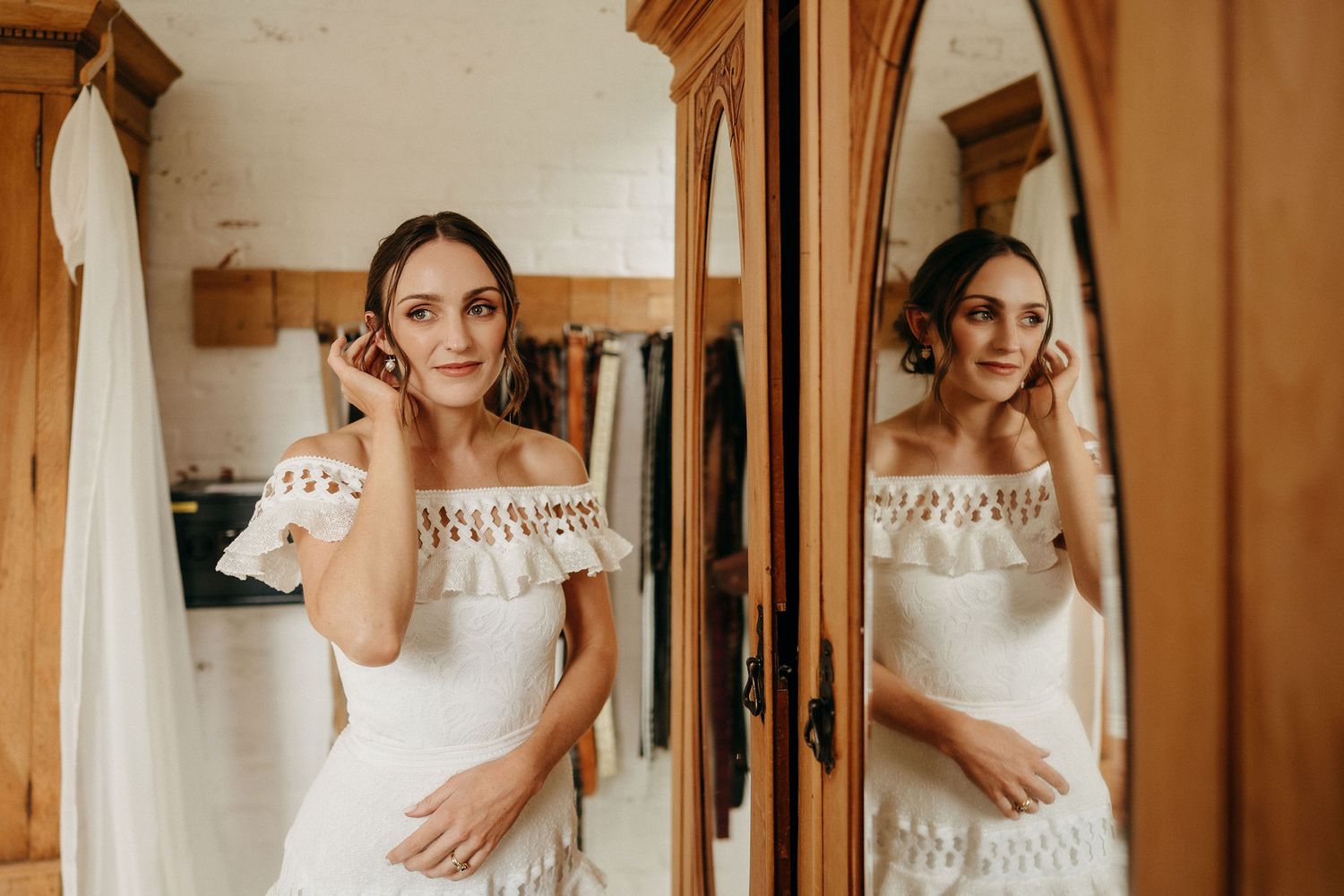 A reflection in an ornate wooden mirror shows a white off-shoulder lace wedding dress.
