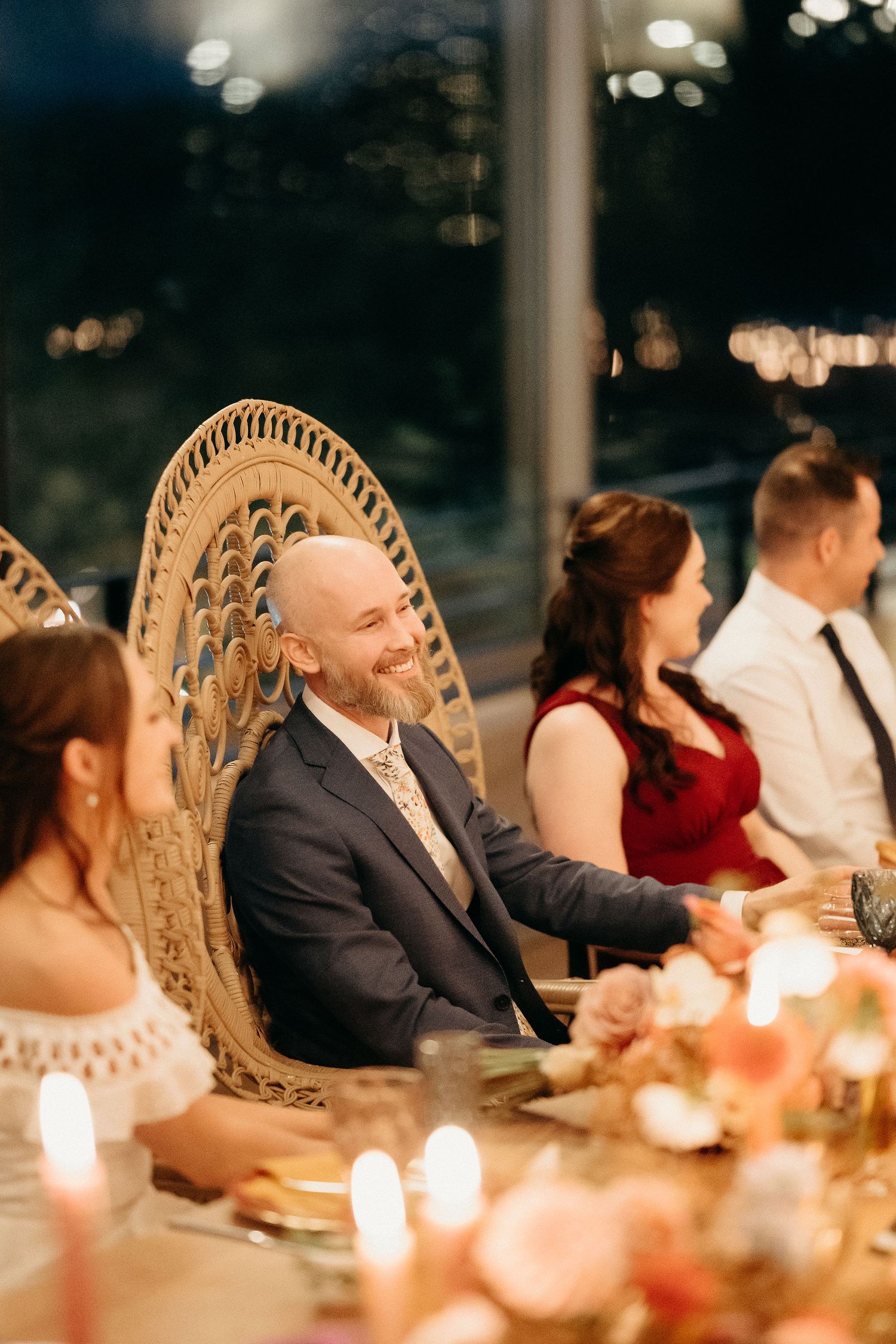 Elegant dinner party setting with wicker peacock chair and candlelit table decorated with warm ambient lighting.