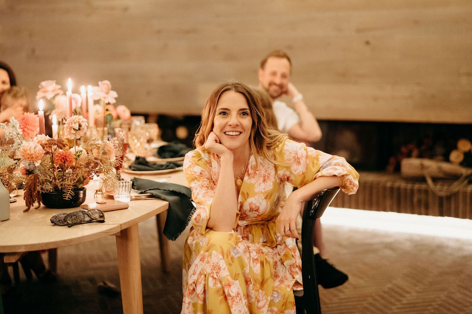 A festive dinner party featuring candles and floral centerpieces in a warm-lit rustic indoor setting.