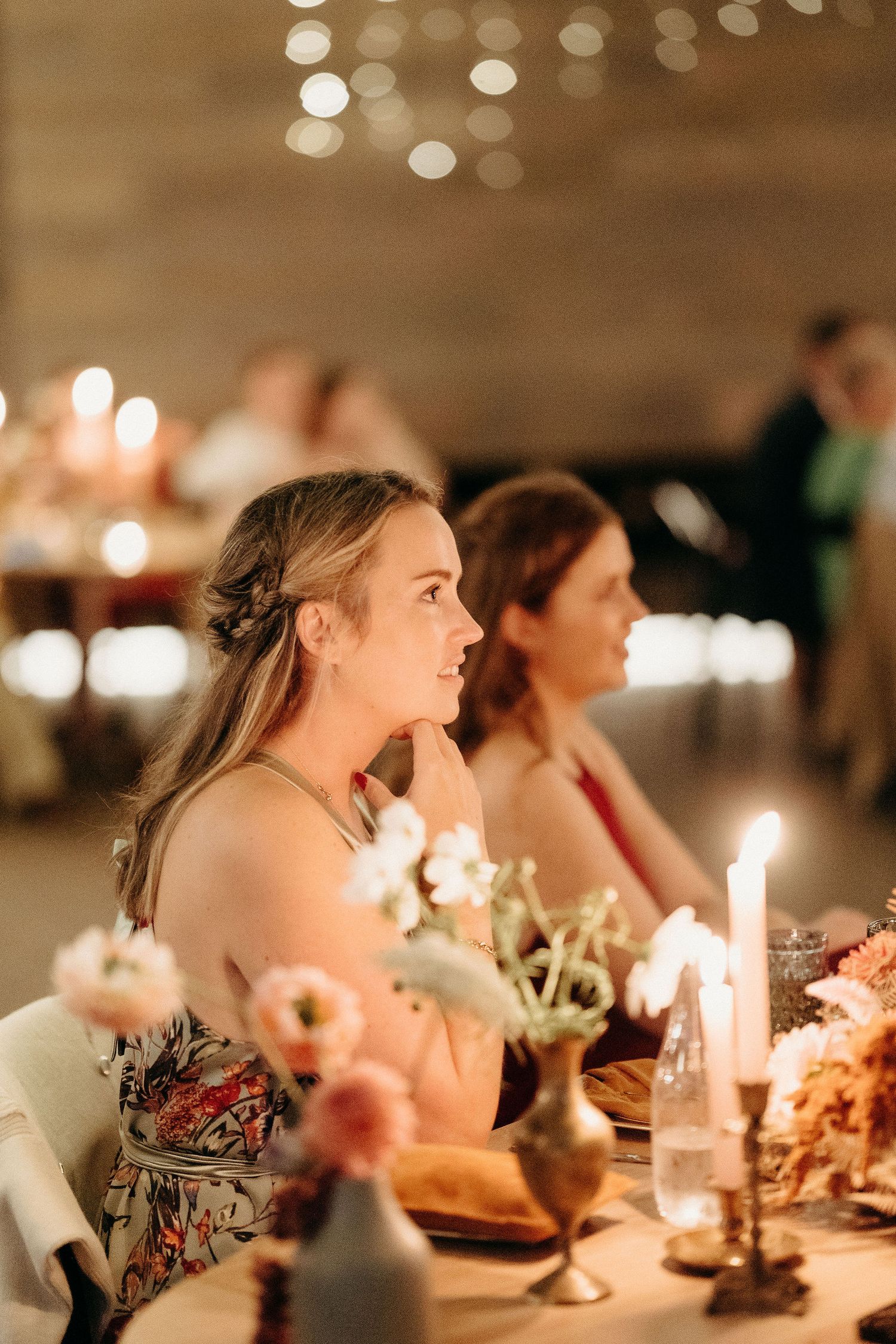 Guests enjoy an elegant candlelit dinner with floral centerpieces and warm ambient lighting at a wedding reception.