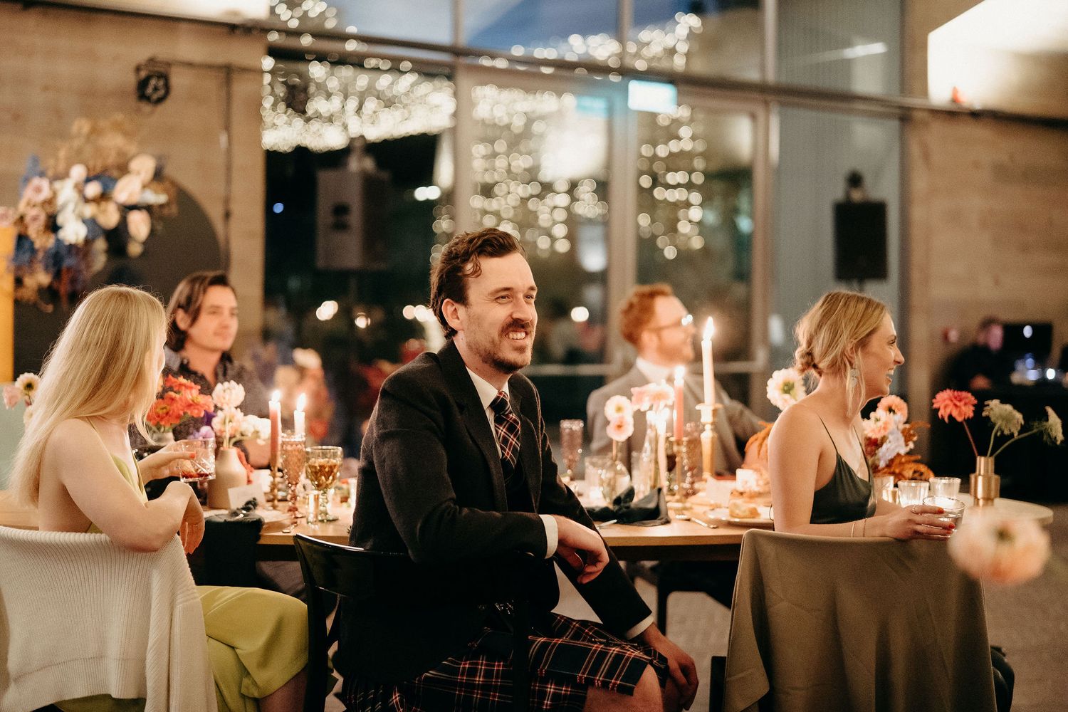 People enjoying an elegant candlelit dinner party in a dimly lit restaurant with festive decorative lights.