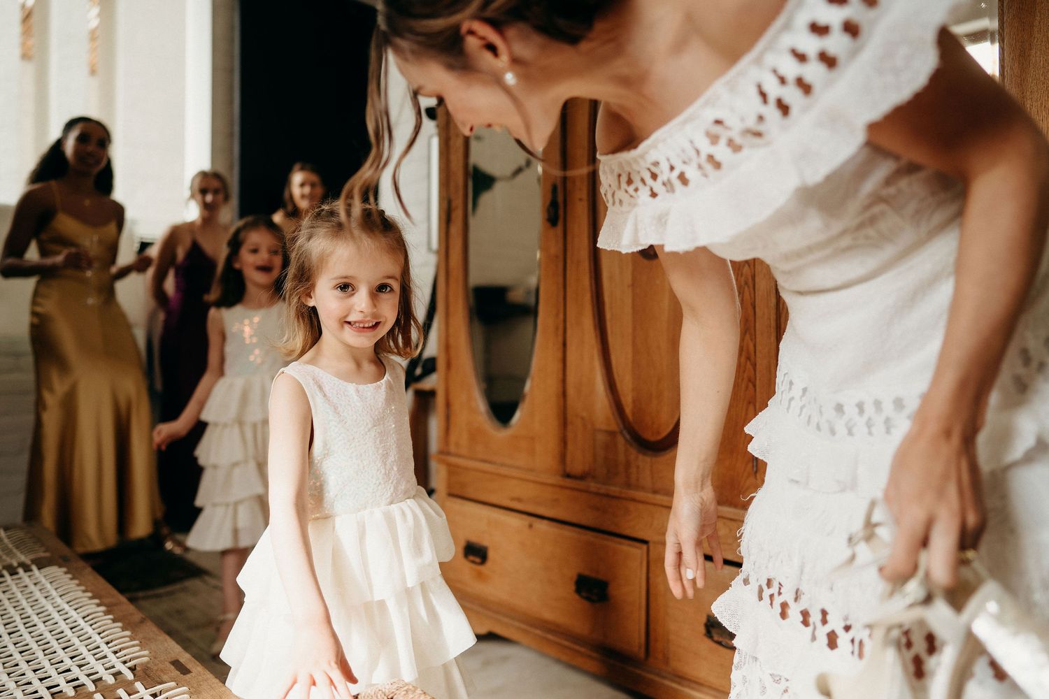Little girl in white dress admires a bride's lace gown during wedding preparations.