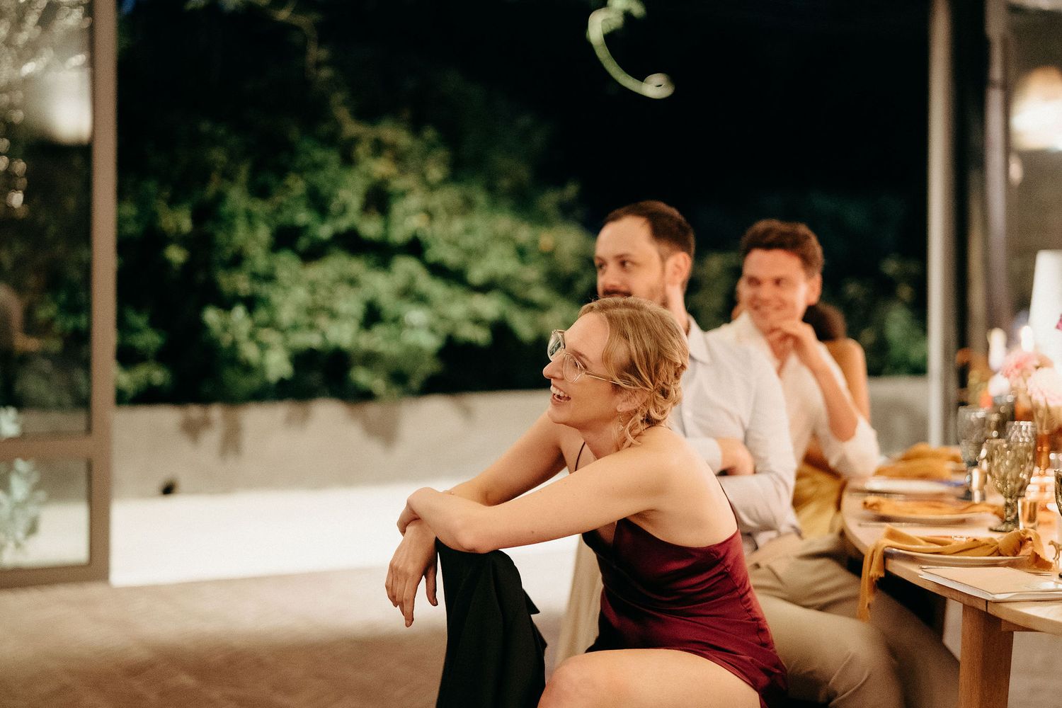 People enjoying a festive evening gathering at an outdoor dinner party with warm lighting and decorative table settings.