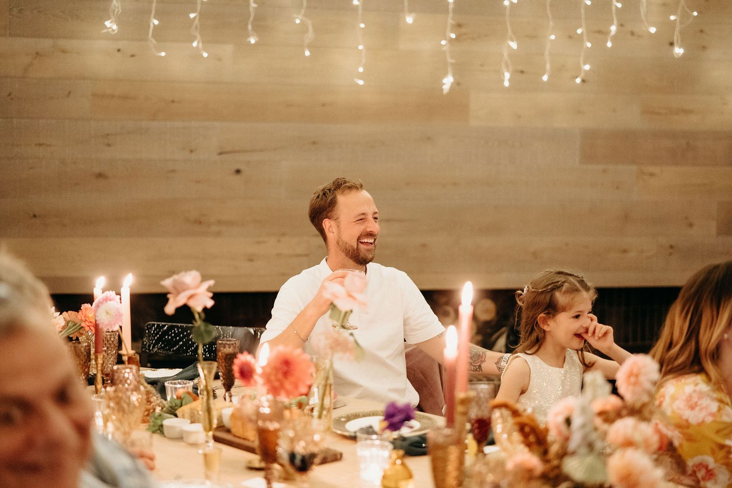 A joyful dinner party celebration with twinkle lights overhead and guests gathered around a long table.