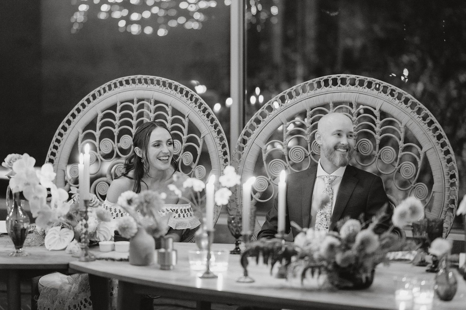 A black and white wedding reception photo showing elegant peacock chair decor and floral centerpieces at the sweetheart table.