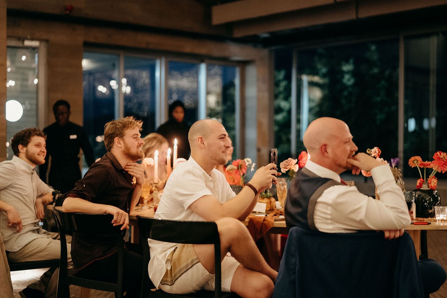 People sit and watch attentively in a room with warm lighting during what appears to be a presentation or event.