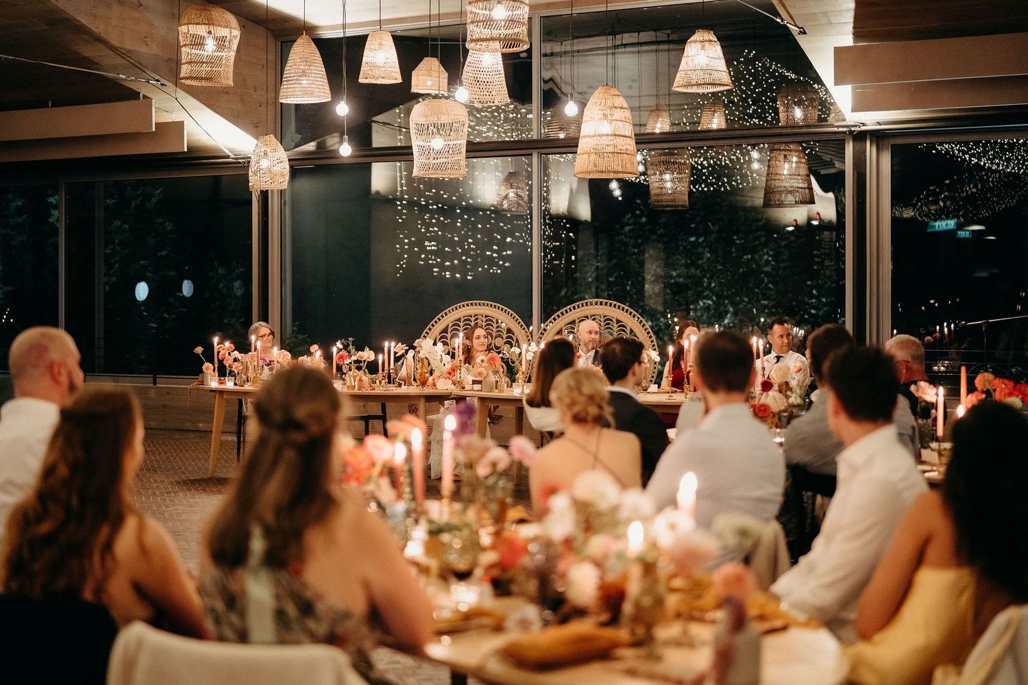 Guests seated at an elegant candlelit wedding reception with hanging pendant lights and warm ambient lighting.
